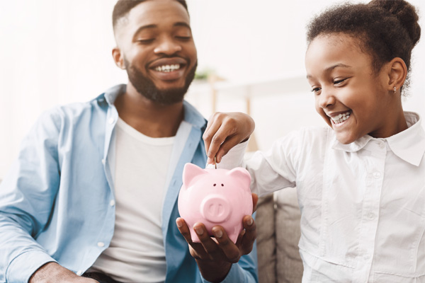 Father and daughter adding money to her piggy bank