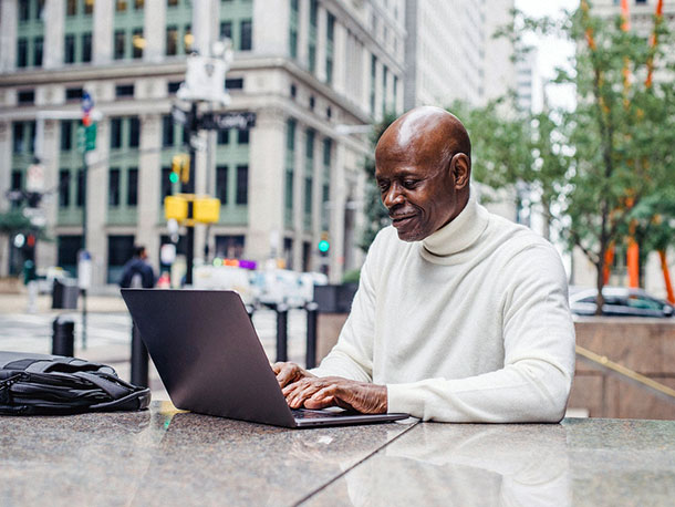 Smiling black business man with laptop on street