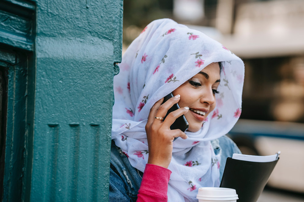 Smiling ethnic woman talking via modern smartphone in city street