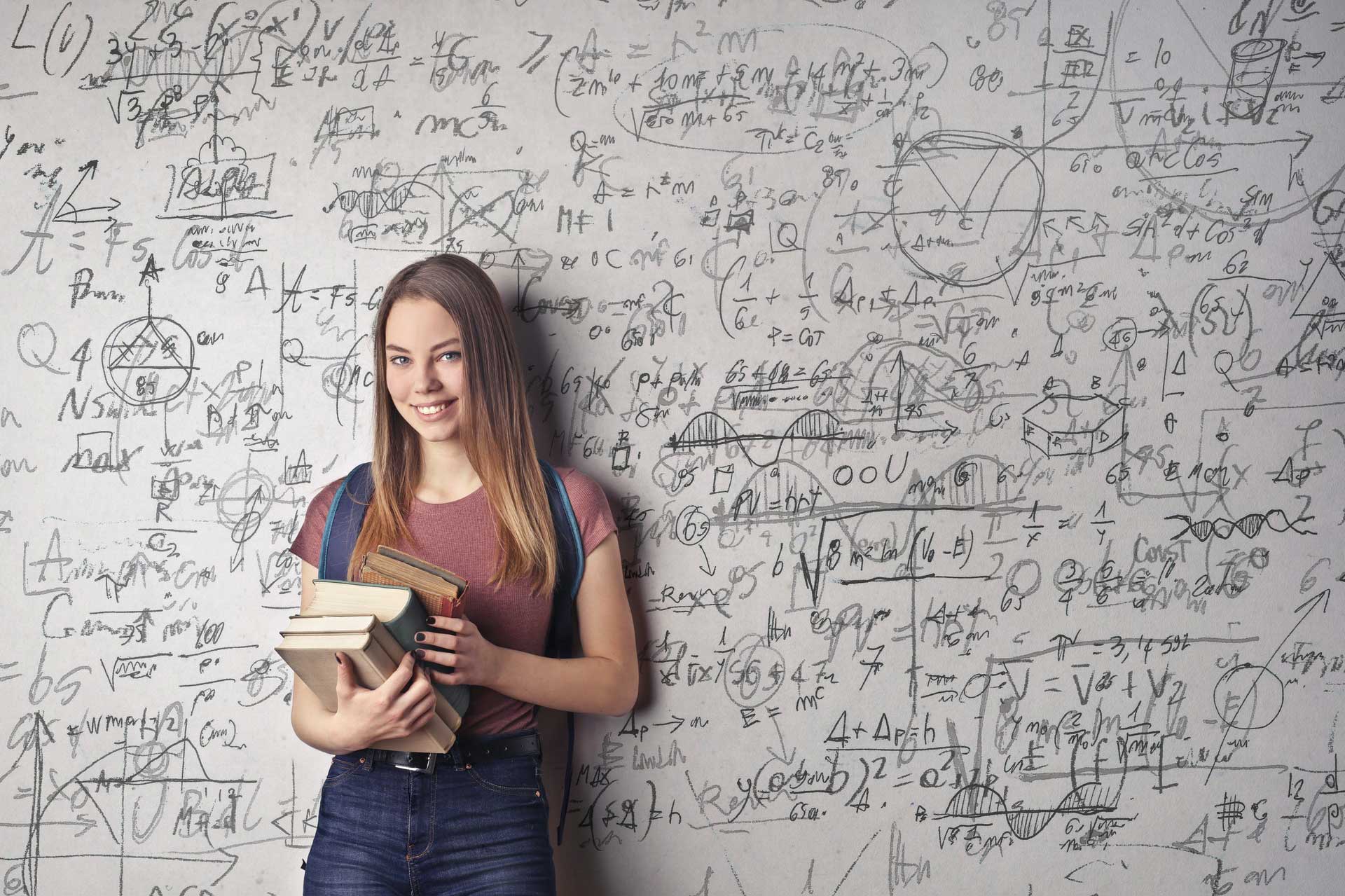 Smiling Female student holding books next to whiteboard
