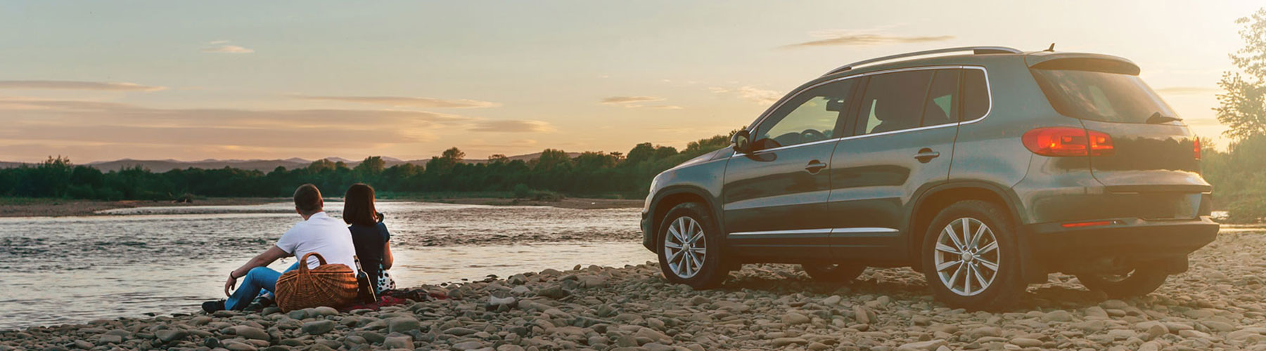 Vehicle parked on the shore of a small lake with a couple sitting on the ground next to it