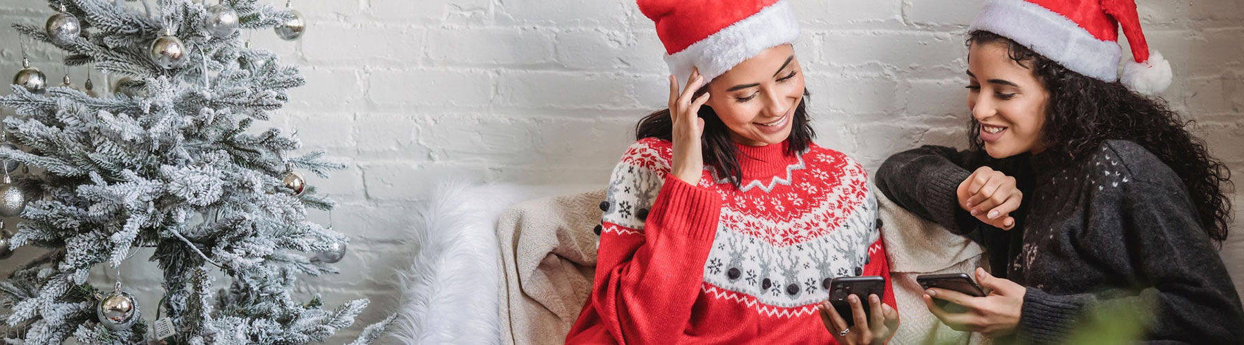 Cheerful women in Santa hats using smartphones together Cheerful women in Santa hats using smartphones together