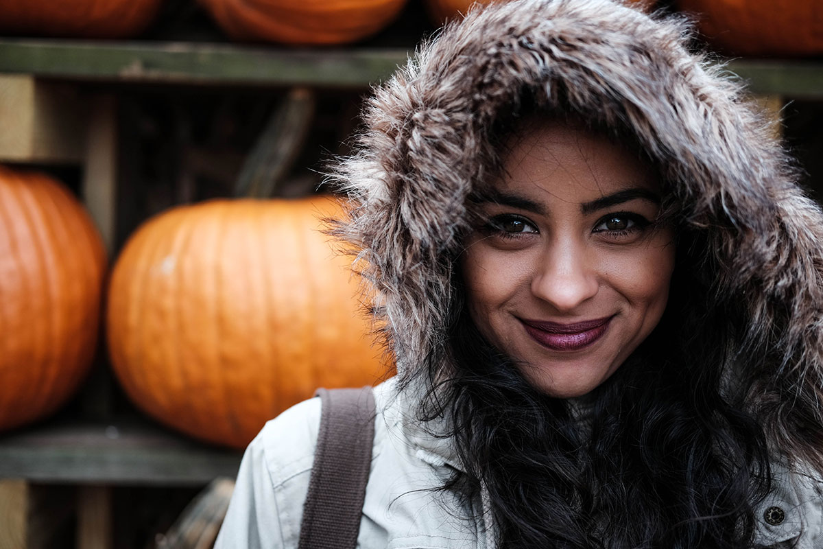 Female wearing a jacket standing in front of pumpkins and smiling