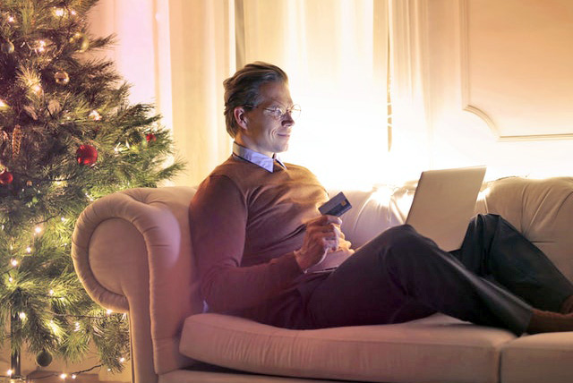 Man sitting on couch with laptop and credit card by Christmas tree