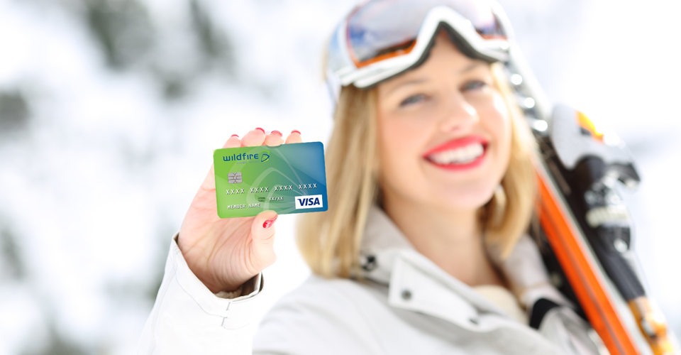 Smiling female carrying snow skis and showing a Wildfire Visa Credit Card