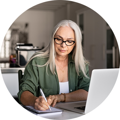 Senior female writing notes while on computer