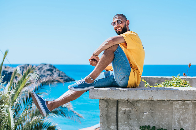 Smiling man in sunglasses sitting on a ledge while on vacation in the tropics