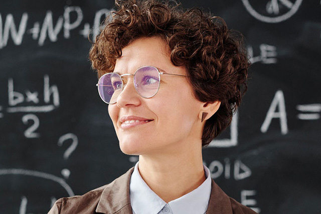 female teacher looking on hopefully with chalkboard behind her