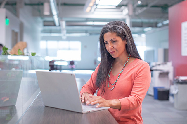 middle aged woman in orange long sleeve shirt using laptop in an office space
