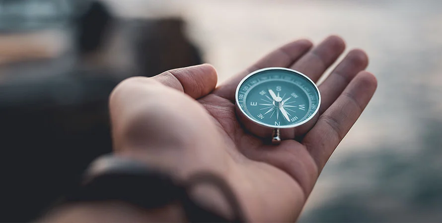 A hand holding a compass with blurry background.
