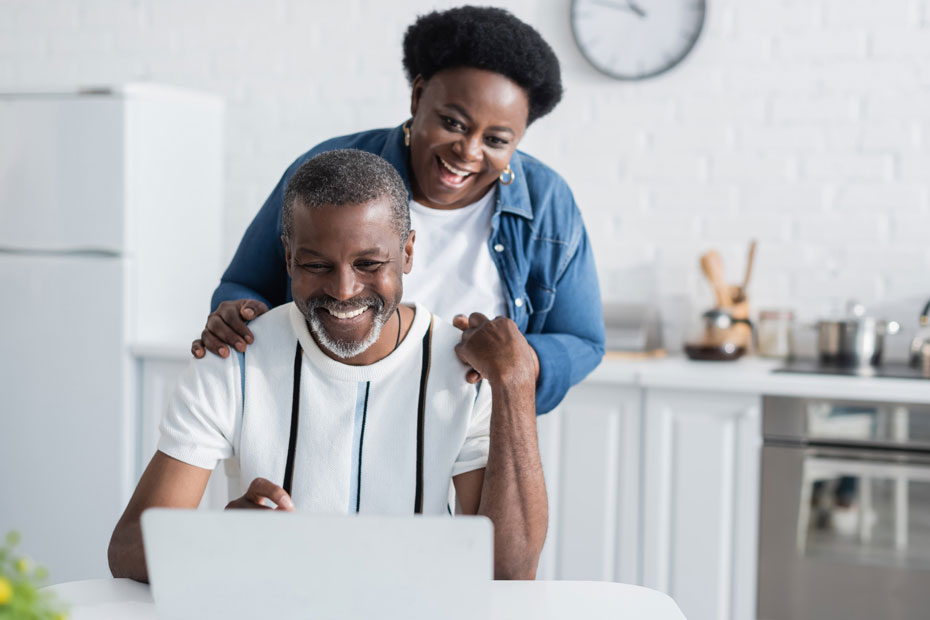 Couple smiling while looking at their laptop in bright white kitchen.