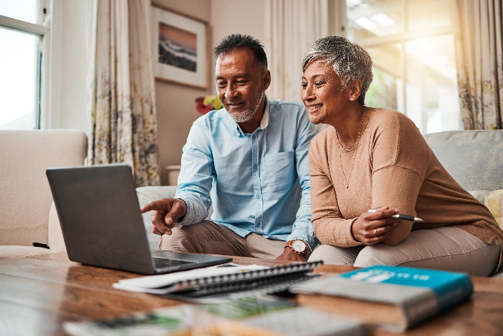 Couple pointing to laptop on table in a warm living room and sitting on the couch with sun shining through.