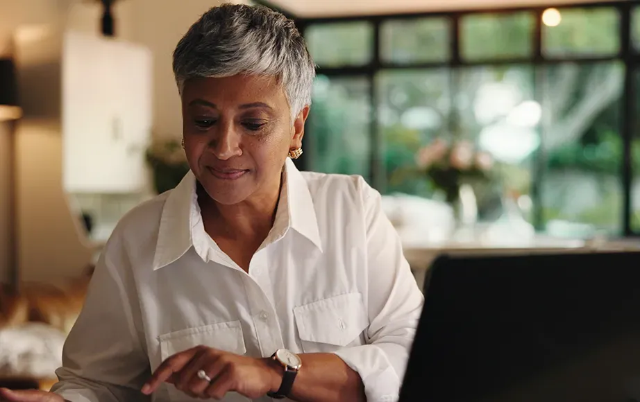 Woman on her computer in kitchen with plants in the background.